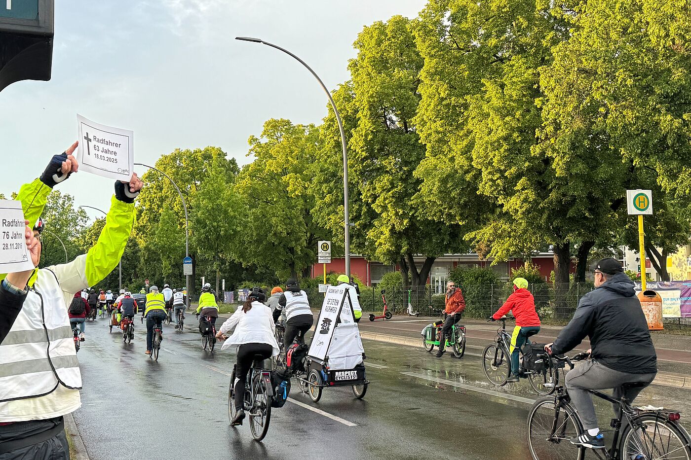 Menschen halten zwei weiße Gedenkschilder bei Fahrraddemonstration in die Luft