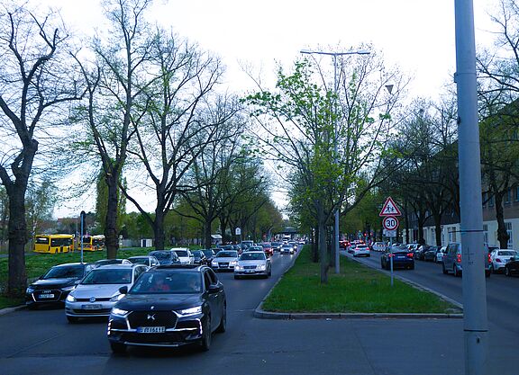 Foto vom Tempelhofer Damm, vom begrünten Mittelstreifen aus Richtung Süden betrachtet. Rechts und links fahren auf jeweils zwei Fahrspuren Autos. Sowohl auf dem Mitteistreifen als auch am Fahrbahnrand stehen Bäume.