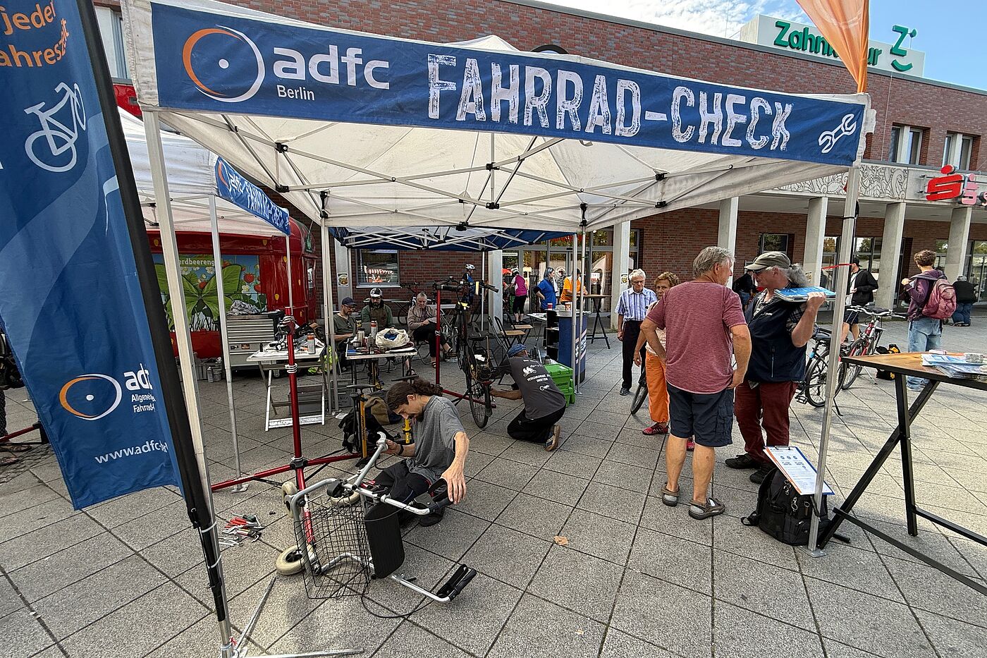 ADFC-Fahrrad-Check Pavillon mit Menschen die sich unterhalten und ein Mechaniker, der einen Rollator repariert