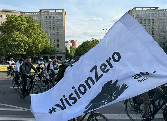 weiße Vision Zero Fahne weht vor Radfahrenden 