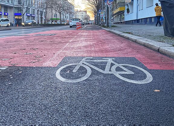 Auf der Fahrbahn der Grunewaldstraße ist ein geschützter Radweg mit Baken, roten Markierungen und einen Fahrradpiktogramm versehen.
