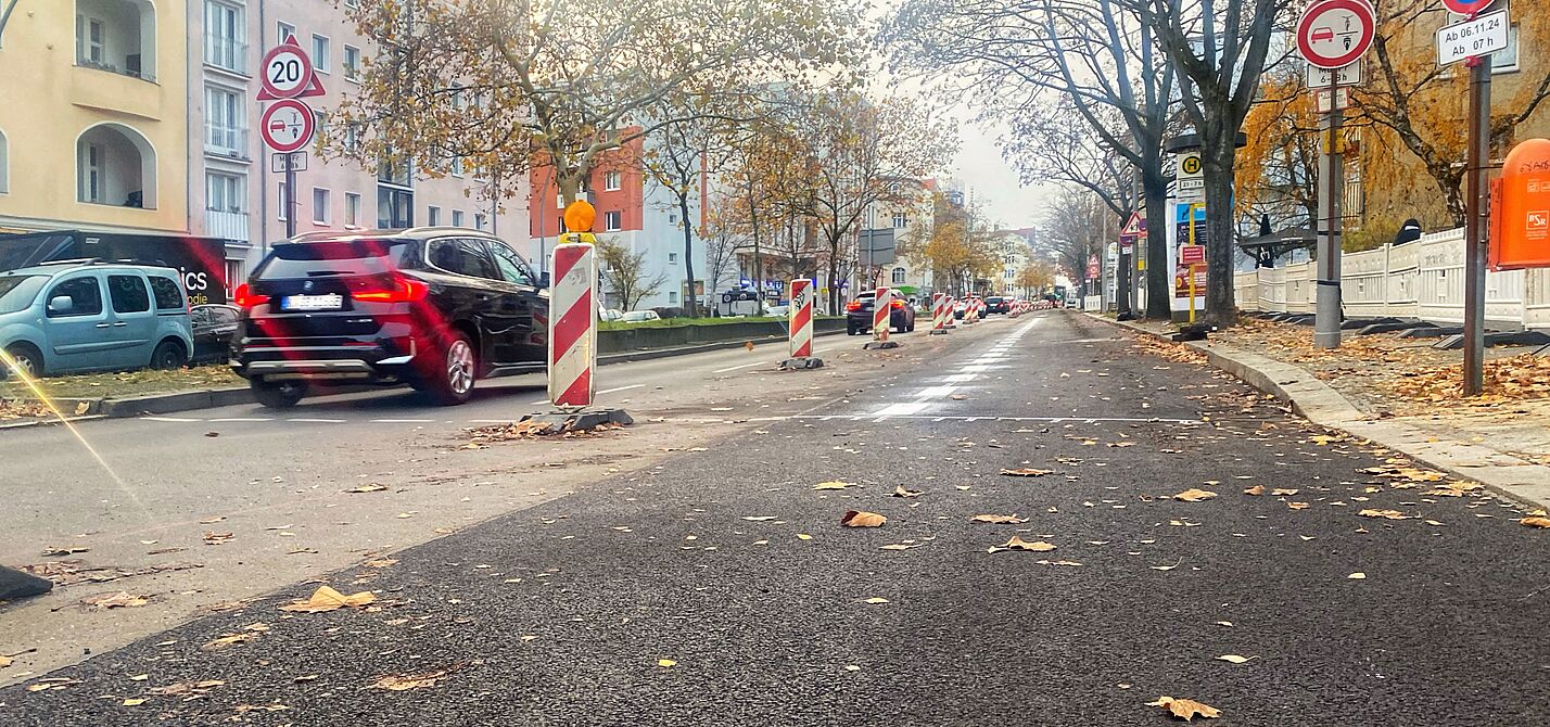 Auf der Grunewaldstraße entsteht ein geschützter Radstreifen Zwischen Martin-Luther-Straße und Bayerischem Platz ist eine frisch asphaltierte Fahrbahn am rechten Rand durch einen weißen Streifen und Baken von der Spur für Autos weiter in der Mitte abgegrenzt.