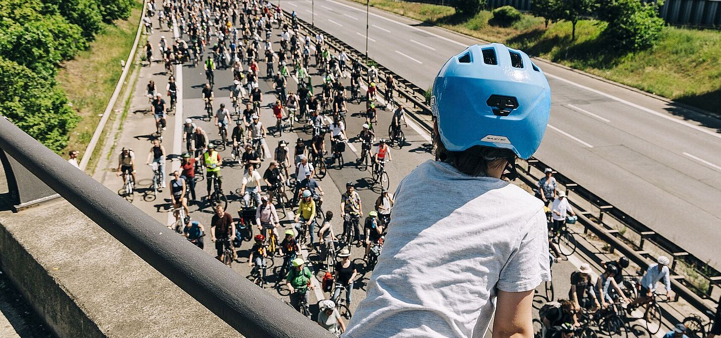 Kind mit blauem Helm guckt auf Autobahn über die auf einer Seite hunderte FahrradfahrerInnen fahren