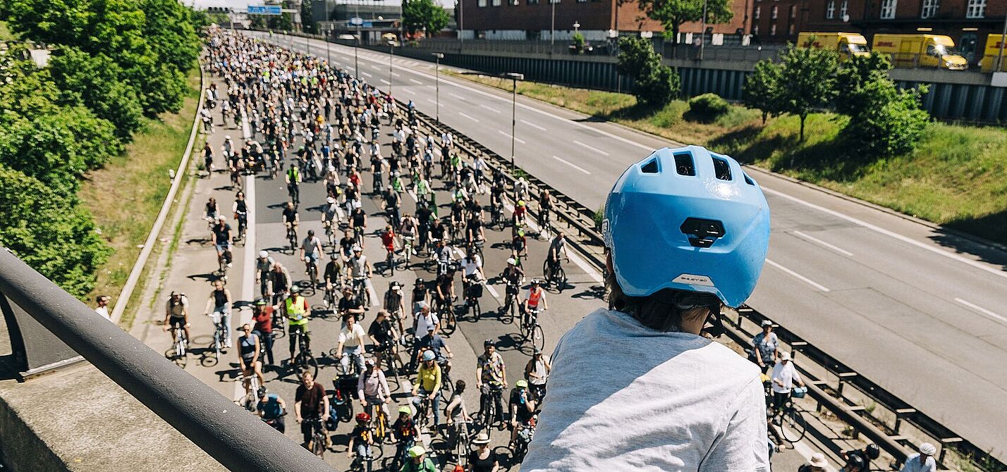 Kind mit blauem Helm guckt auf Autobahn über die auf einer Seite hunderte FahrradfahrerInnen fahren