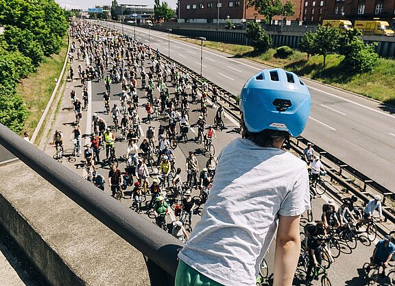 Kind mit blauem Helm guckt auf Autobahn über die auf einer Seite hunderte FahrradfahrerInnen fahren